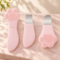 Pink cat paw facial cleansing tool shown closed and opened, with its two metal spatula tips