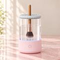 Pink electric makeup brush cleaner with a brush in the lid and its USB cable
